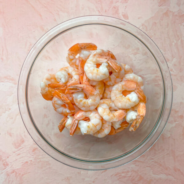 velveted shrimp in a glass bowl on a pink background