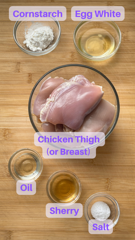 Ingredients for Velvet Chicken arranged in glass bowls on a bamboo cutting board ready to prepare.