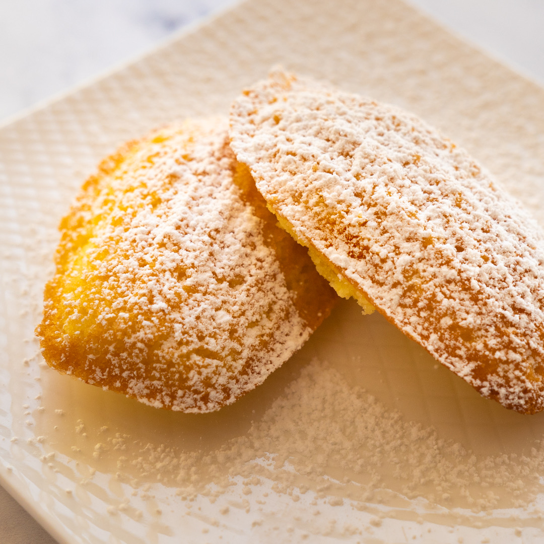 Orange Madeleines on a plate with confectioners’ sugar dusting.