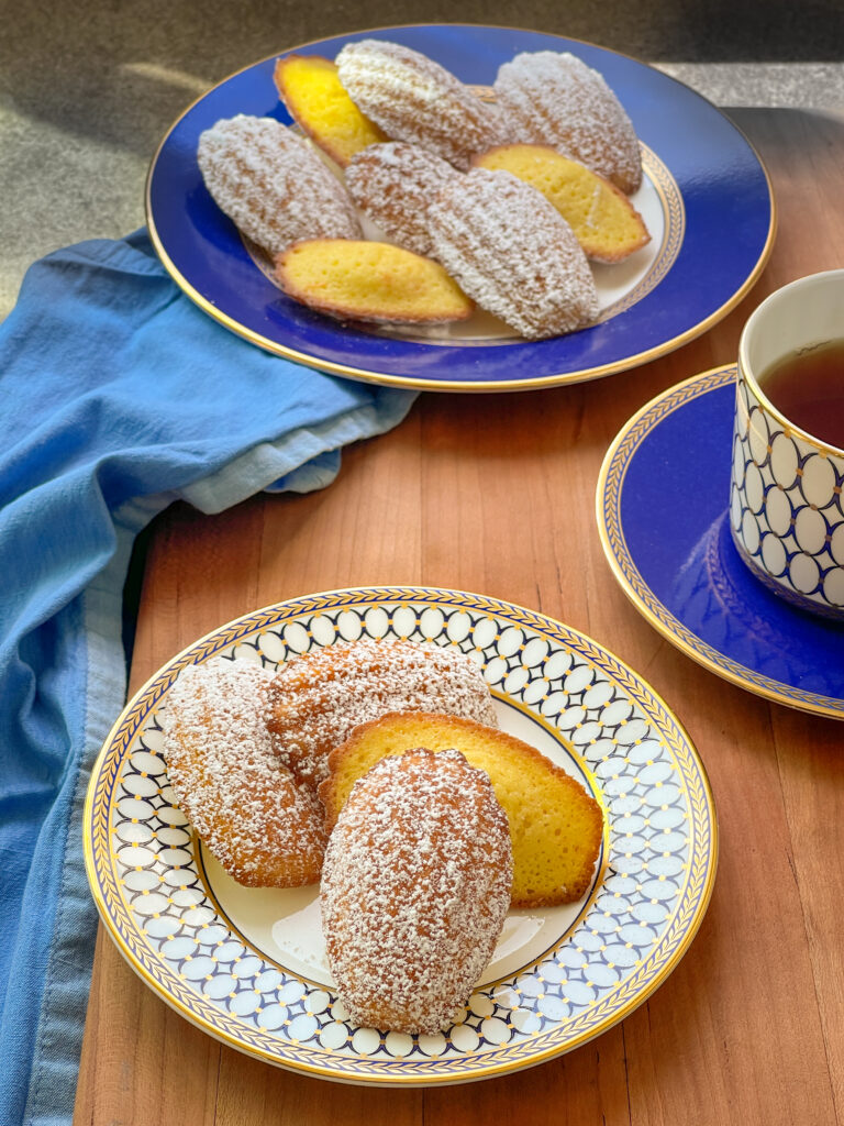 Orange Madeleines on a large serving plate, on a personal small plate, served with a cup of tea, all on a lovely blue wedgewood china set.