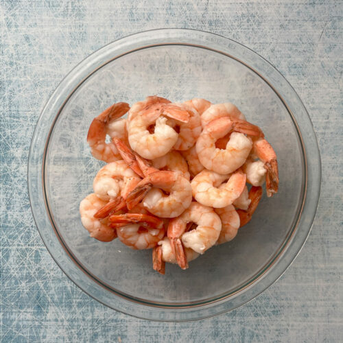 top down picture of shrimp that has been already velveted, on a light blue velvet background, in a glass bowl