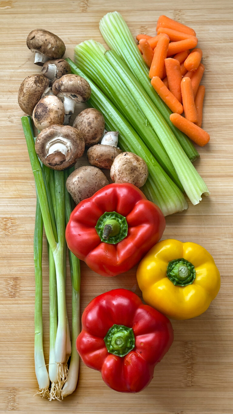 Typical Vegetables like Green Onion, Mushrooms, red and yellow peppers, celery and baby carrots on a bamboo cutting board ready to cut for stir-fry.