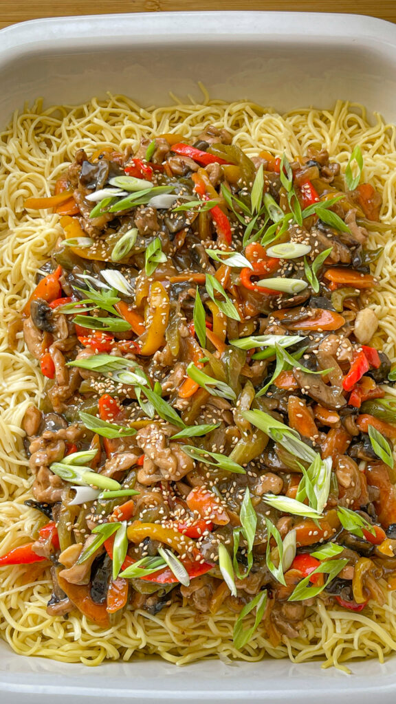 Large Tray of Lo Mein Noodles with Chicken, and Vegetables on top of Noodles, and sprinkled with green onions, and sesame seeds.