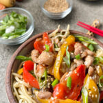 Bowl of Chicken Chow Mein noodles with red and yellow peppers, chicken, topped with green onions and sesame seeds