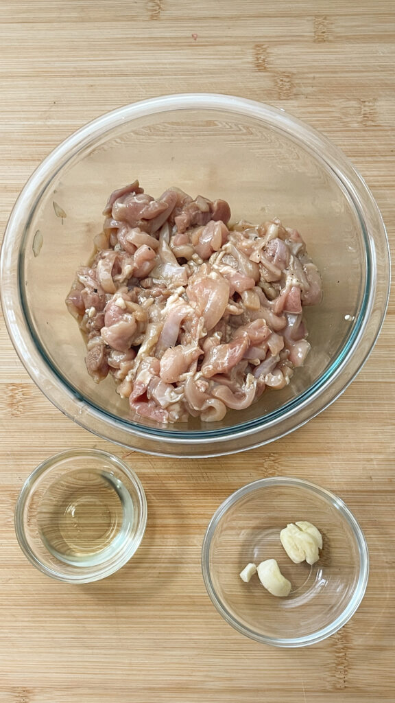 Sliced Chicken, garlic and oil prepped for cookingin glass bowls